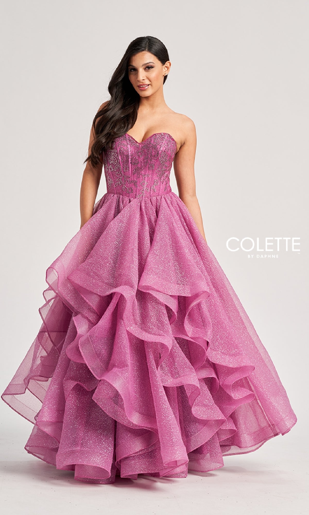 A woman poses in the Colette CL8200 Long Prom Ball Gown featuring a strapless beaded corset bodice and ruffle tiered glitter tulle skirt.